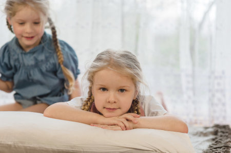 two little girls sisters lie on their stomachs on the floor at home and smileの写真素材