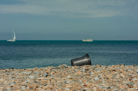 black plastic bucket lying on a rocky beach in summer. garbage on the beach in summer