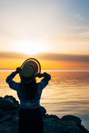 close-up portrait of a woman from the back in a summer hat at sunset on the sea, ocean in travelの写真素材