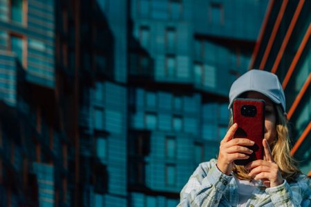 close-up portrait of a woman in the summer on the street against the background of the glass facade of a modern building on a city street with a phone in her handsの写真素材