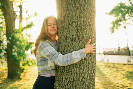 close-up portrait of a smiling young woman hugging a tree in the summer at sunset in the sunの写真素材