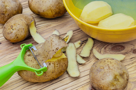 Green peeler and potatoes on wooden backgroundの写真素材
