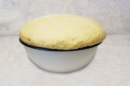 The image shows a bowl of dough that has risen significantly, filling and overflowing the bowl. This marks the first successful steps in the production of bread or baked goods.の写真素材