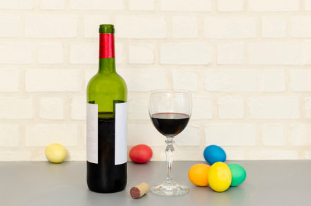 Easter decorations, colorful eggs, a glass of red wine with a bottle, brick wall in background. Copy space for text.の写真素材