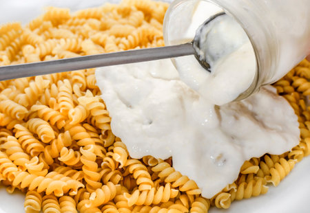 Close-up adding white sauce to a plate of pastaの写真素材