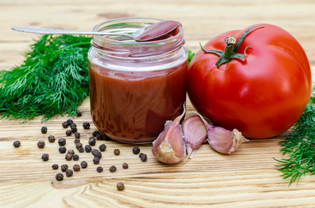 Tomato sauce with garlic, pepper and dill in a glass jar on a wooden tableの写真素材