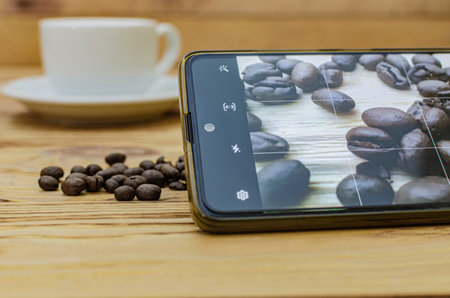 Close-up of a smartphone that takes a picture of spilled coffee beans on a table in a cafeの写真素材