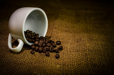Coffee cup with coffee beans upside down on a surface covered with burlapの写真素材
