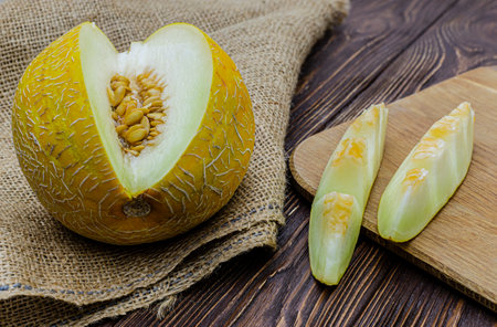 Close-up of a cut melon lying on a wooden table with a burlap bedding, next to a cutting board with fruit slicesの写真素材