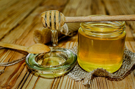 Honey in jar with honey dipper on rustic wooden table background.