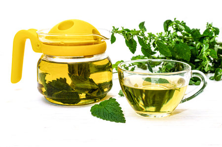 Healthy lemon balm tea natural organic flavored drink in glass cup and teapot on white wooden surfaceの写真素材