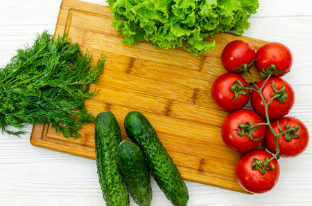 Top view of cutting board with vegetables, tomatoes,cucumbers,dill and lettuce prepared for slicing lettuceの写真素材