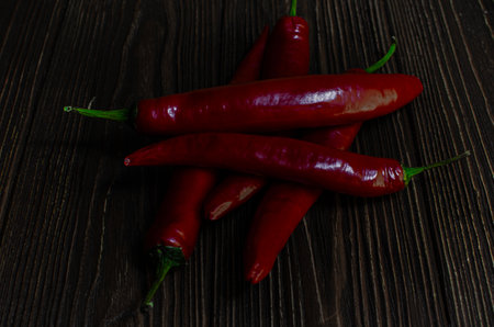 Close-up shot of several red chili peppers scattered on a dark wooden table.の写真素材