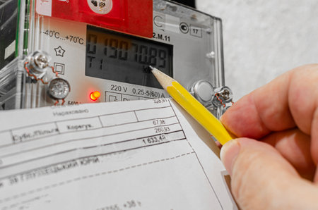Hand with a pencil and a receipt reconciling the readings of the electricity meter at home. Payment of utility services.の写真素材