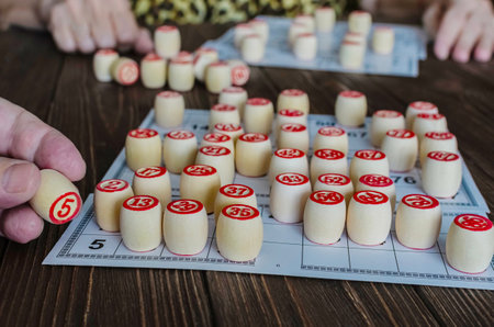 Closeup of hands playing the traditional Loto board game on a dark wooden table.