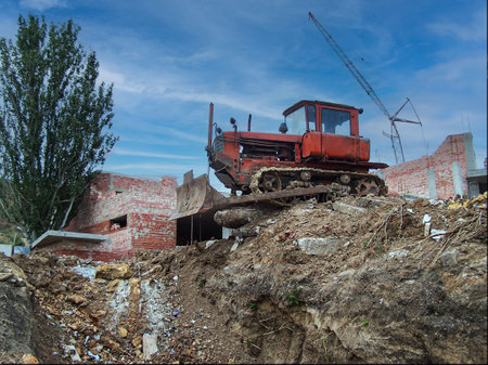 An old red crawler bulldozer (tractor) is parked on a large pile of dirt, bricks and rubble at an active construction or demolition site.の写真素材