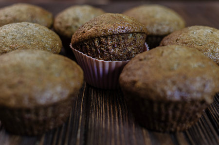 Close-up of freshly baked chocolate cupcakes, one of which is highlighted in a pink baking pan, placed on a dark wooden surface. Shallow depth of field.の写真素材