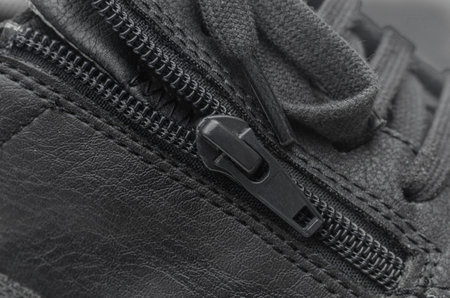 A close-up macro shot of a black zipper on a black leather shoe, highlighting the texture of the material and the detail of the fastener.の写真素材