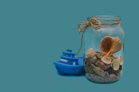 A still life composition featuring a glass jar filled with seashells and sand, symbolizing summer memories.の写真素材