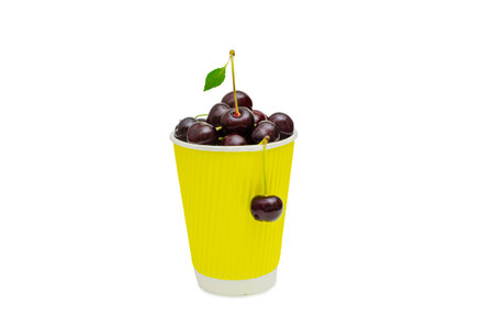 A vibrant yellow paper cup filled with fresh dark red cherries, isolated on a white background. One cherry with a stem and leaf stands out on top, while another hangs from the cup's edgeの写真素材