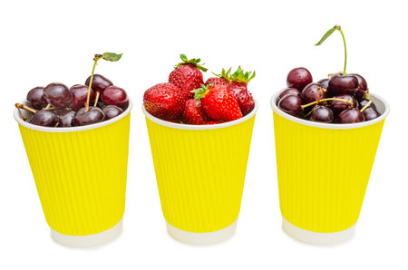 Three vibrant yellow paper cups are filled to the brim with fresh, ripe berries. Two cups contain dark red cherries, some with their green stems still attached, while the middle cup overflows with bright red strawberries.の写真素材