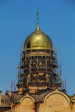 A detailed view of a golden dome on an Orthodox church under restoration, surrounded by wooden scaffolding against a clear blue sky.の写真素材