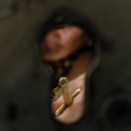 A close-up view of a hand holding an old-fashioned brass key, seen through a large keyhole, creating a sense of mystery and anticipation.の写真素材