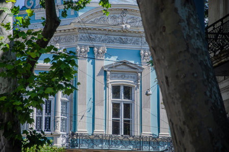 A captivating view of a beautiful, light blue historic mansion in Odesa, Ukraine, featuring ornate classical architecture, a decorative balcony, and large windows, framed by lush green trees.の写真素材