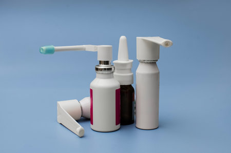 A collection of various medical spray bottles, including throat and nasal sprays, neatly arranged on a solid blue background.の写真素材