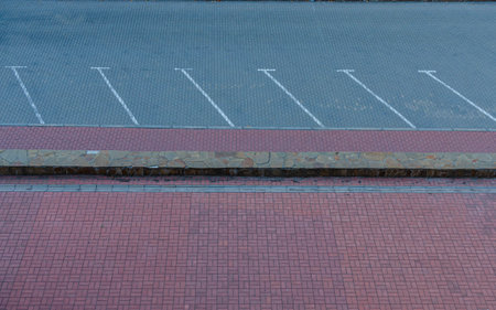 Top view of an empty parking lot with white parking space markings, stone border, and red brick pavement.の写真素材