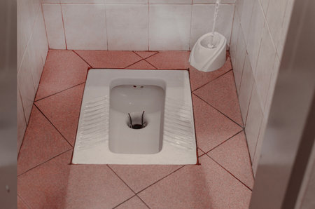 An overhead view of a simple, ceramic squat toilet set into a tiled floor in a public restroom or lavatory cubicle.の写真素材