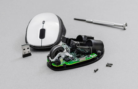 A close-up studio shot of a disassembled wireless computer mouse showing its internal circuit board,...
