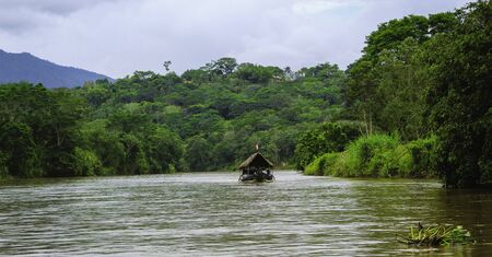 Landscape of a boat driving in the middle of river with a group of people. River has green plants on its sides.の写真素材