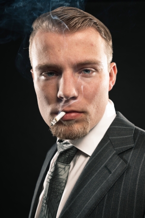 Fashion man in suit smoking cigarette. Studio shot against black.の写真素材