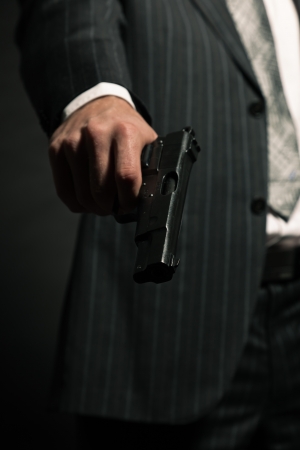 Man in suit shooting with gun  Studio shot against black の写真素材