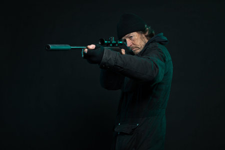 Sniper with beard in black holding gun. Studio shot.