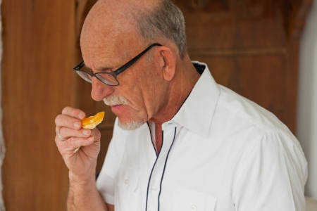 Senior man eating fresh fruit dish. Sitting in living room.の写真素材