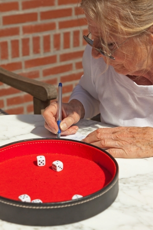 Senior woman writing his score on paper outdoor in garden Playing Yahtzee.の写真素材