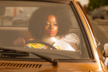 Retro 70s fashion african american woman driving in gold seventies car.の写真素材