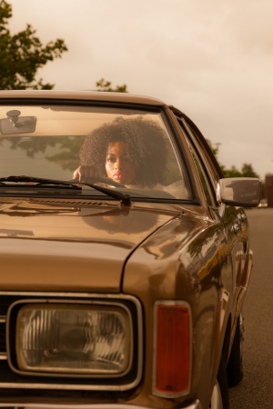 Retro 70s fashion african american woman driving in gold seventies car.の写真素材