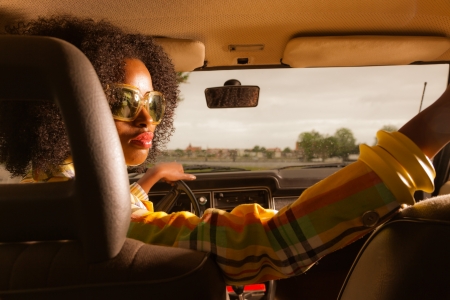 Retro 70s afro fashion woman with sunglasses driving in brown seventies car.の写真素材
