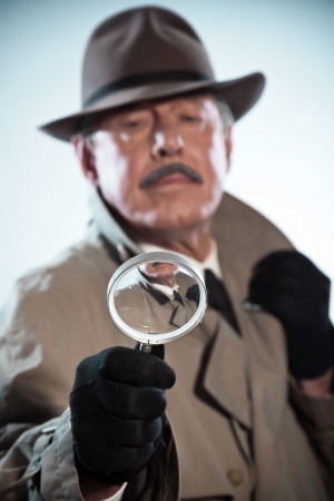 Retro detective with mustache and hat. Looking through magnifying glass. Studio shot.の写真素材