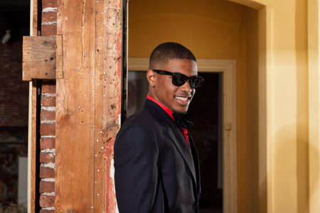 Retro fashion afro american groom wearing black suit and tie and sunglasses. Interior of old house.