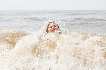 Kid boy having fun at the beach in the waves of the ocean.の写真素材