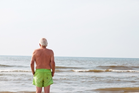 Single senior retired man standing on the beach looking at the ocean.の写真素材