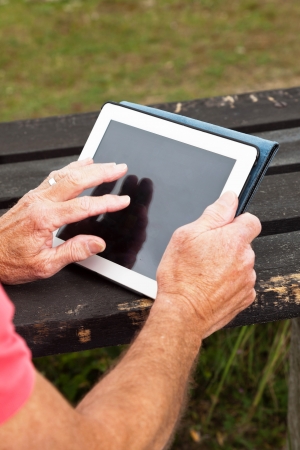 Close-up of hands of retired senior man resting and using his tablet at table in grass dune landscape.の写真素材