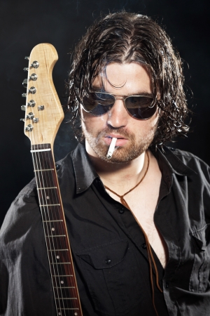 Rock guitarist with long brown hair and beard and sunglasses dressed in black. Smoking a cigarette.の写真素材