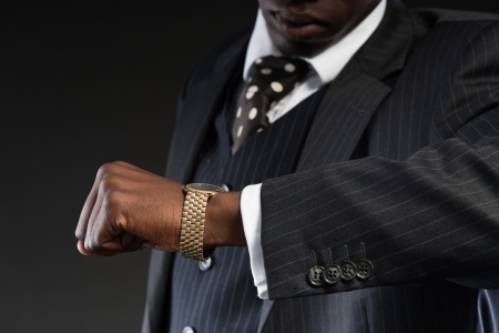Retro african american gangster wearing striped suit and tie and black hat. Looking on his watch. Studio shot.の写真素材