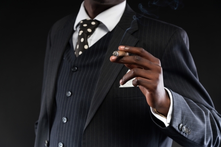 Close-up of hand of retro african american mafia man wearing striped suit and tie. Smoking cigar. Studio shot.の写真素材
