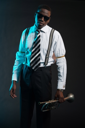 Retro african american jazz musician holding his trumpet. Wearing shirt and tie and sunglasses. Studio shot.の写真素材